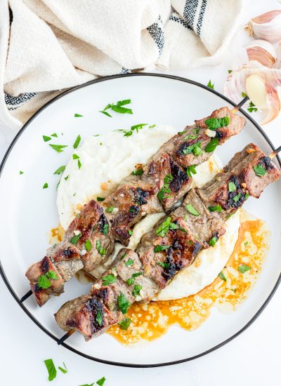 Two steak kabobs on a pile of mashed potatoes on a plate.