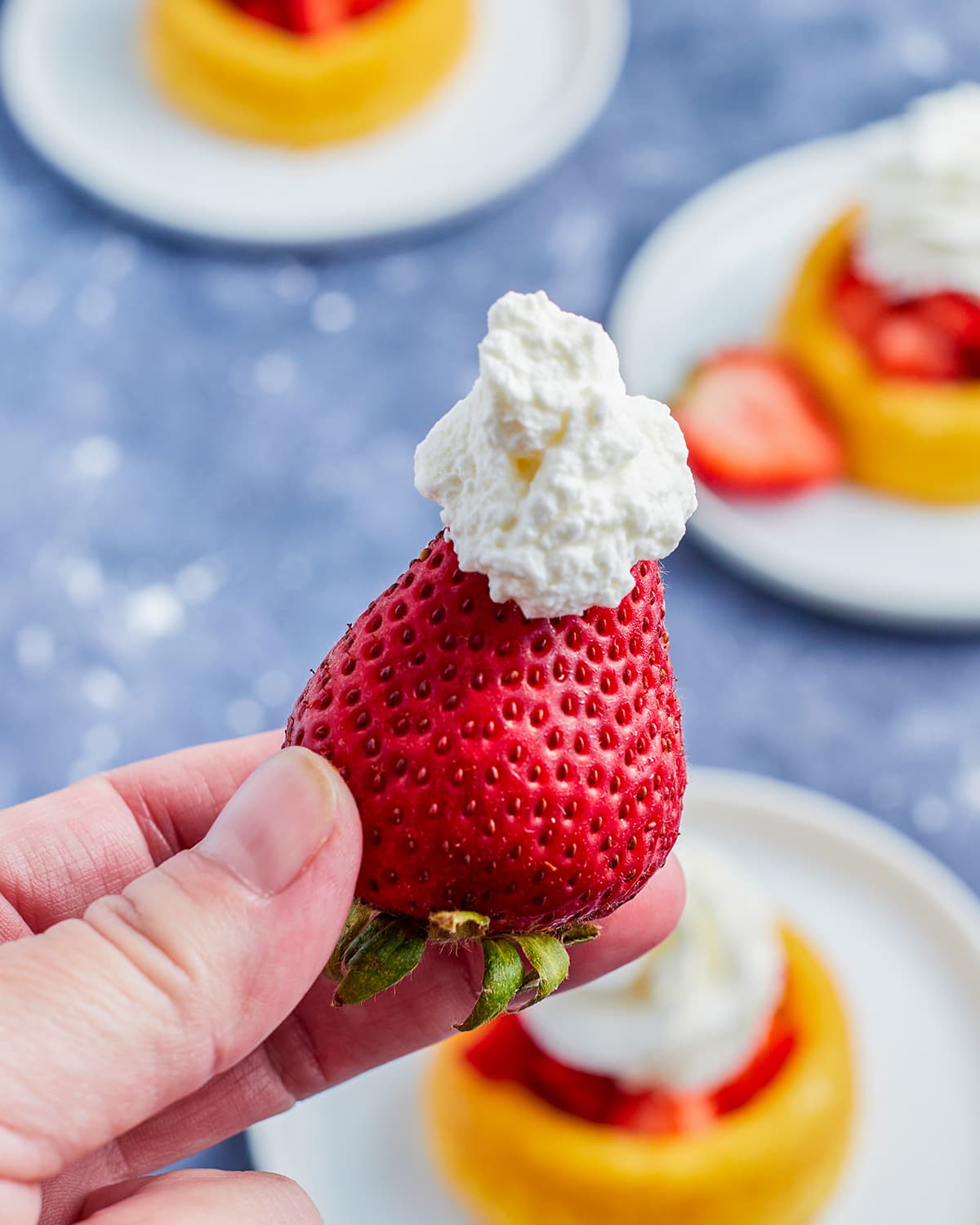 A hand holding a strawberry with whipped cream on top. 