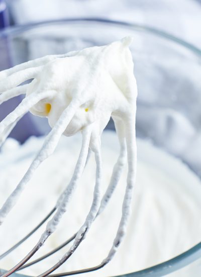 A whisk with stiff whipped cream on it.