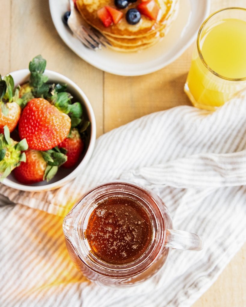 An overhead photo of a pitcher of maple syrup and a bowl of strawberries.