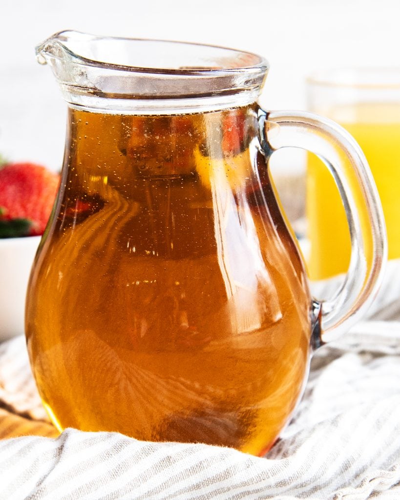 A small glass pitcher full of maple flavored syrup.