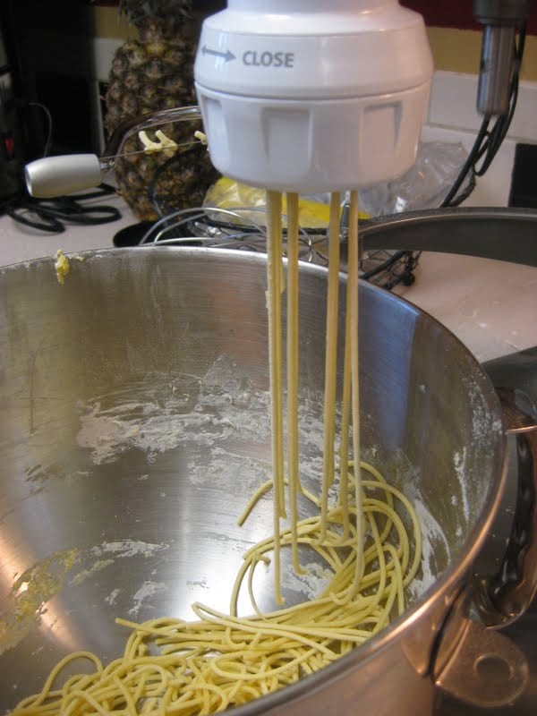 A pasta maker with spaghetti noodles hanging out the bottom of it.
