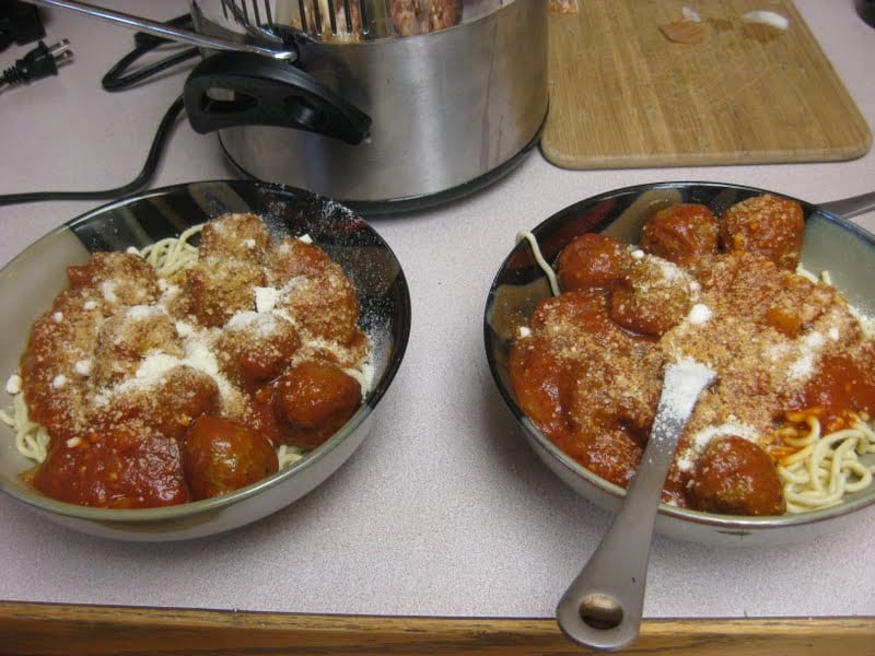 Two bowls of spaghetti and meatballs topped with parmesan. 