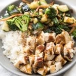 A  bowl of chicken, sauteed veggies, and rice topped with teriyaki sauce.