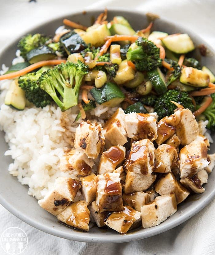A  bowl of chicken, sauteed veggies, and rice topped with teriyaki sauce.