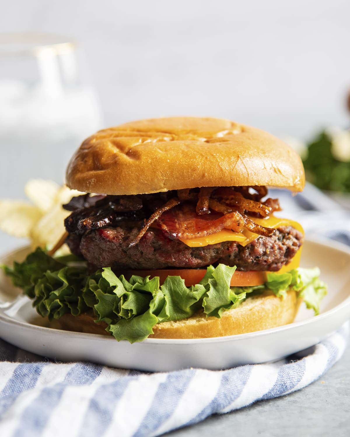 A burger with lettuce, tomato, patty, cheese, brown sugar bacon, and carmelized onions on a bun.