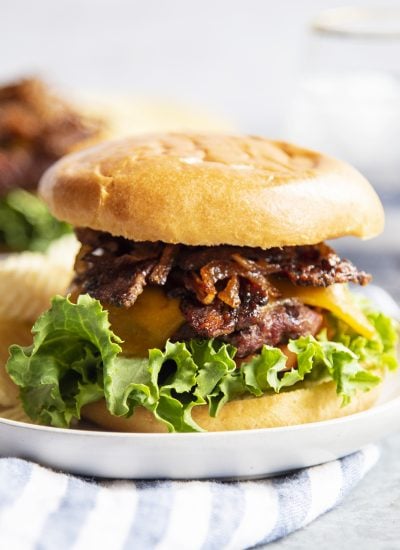 A cheeseburger topped with brown sugar bacon and caramelized onions on a white plate.