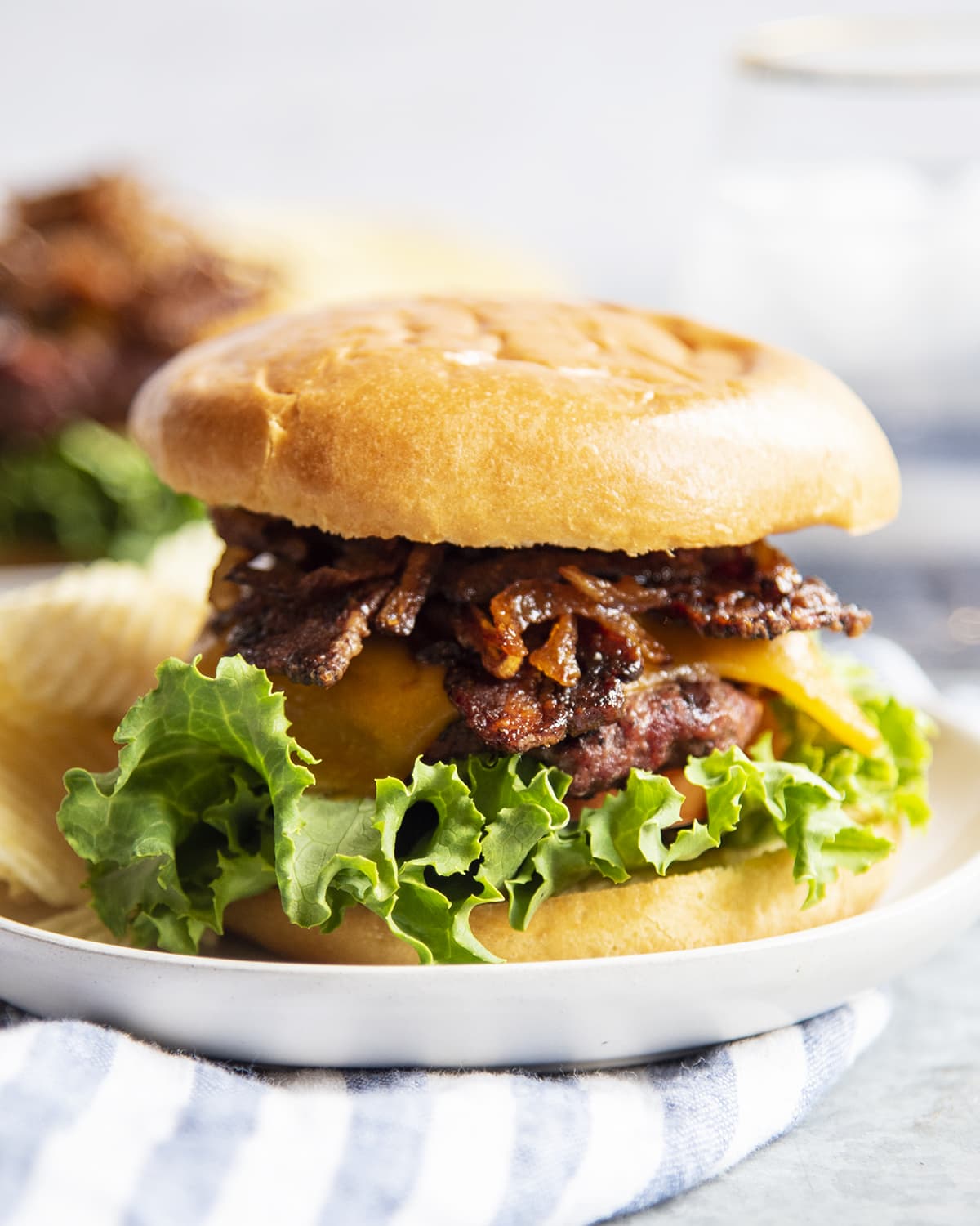 A cheeseburger topped with brown sugar bacon and caramelized onions on a white plate.