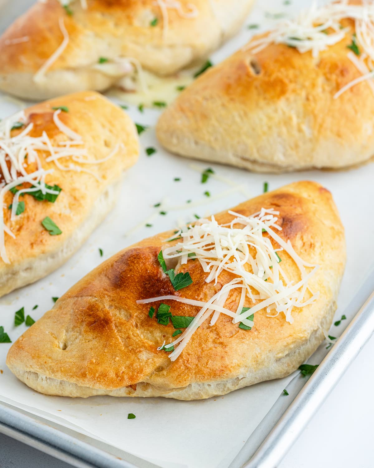 A golden brown calzone on a baking sheet topped with parsley and shredded parmesan.