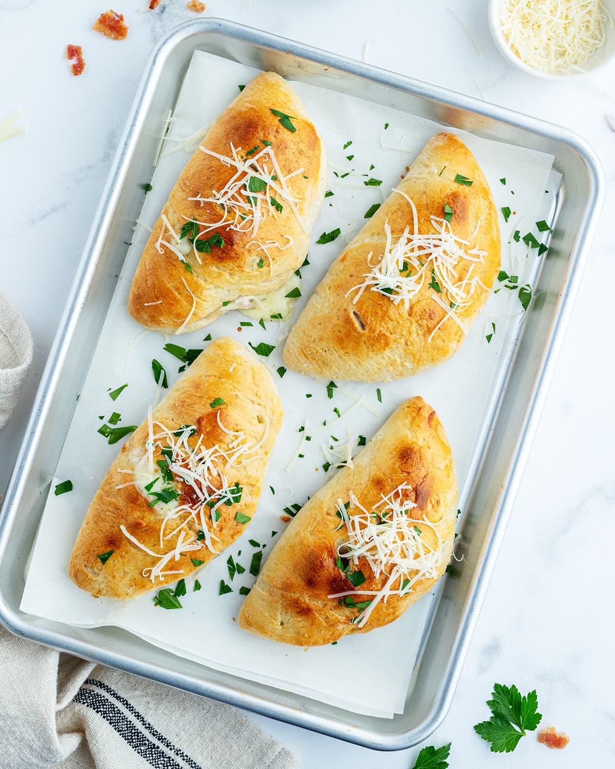 Four calzones on a baking sheet topped with shredded parmesan. 