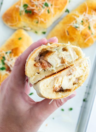 A hand holding two halves of a chicken bacon calzone showing the chicken in the middle.