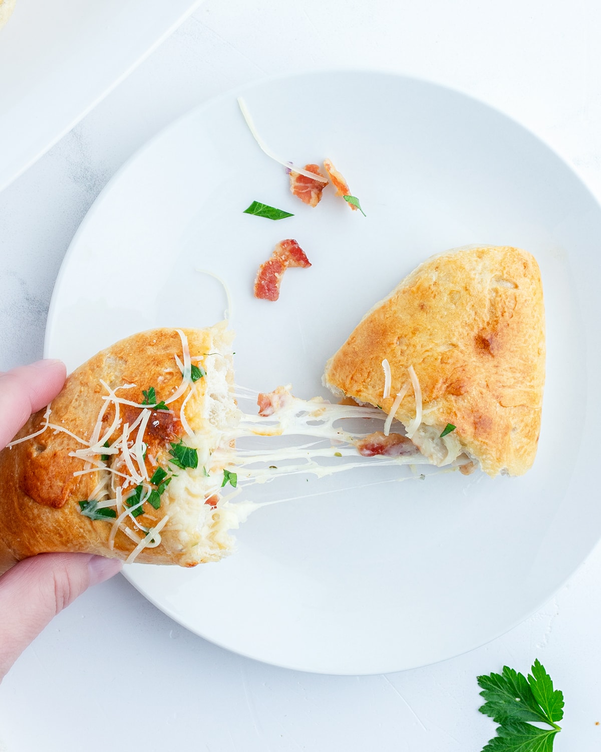 A hand pulling half a chicken bacon ranch calzone off a plate.