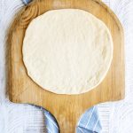 Round pizza dough on a wooden pizza peel.