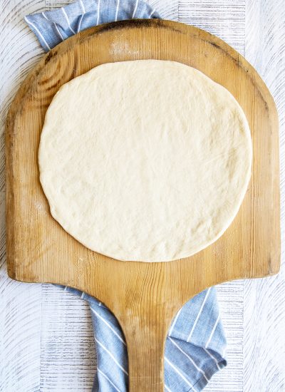 Round pizza dough on a wooden pizza peel.