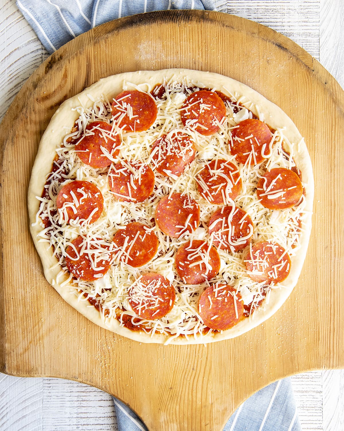 An uncooked pepperoni pizza on a wooden board.