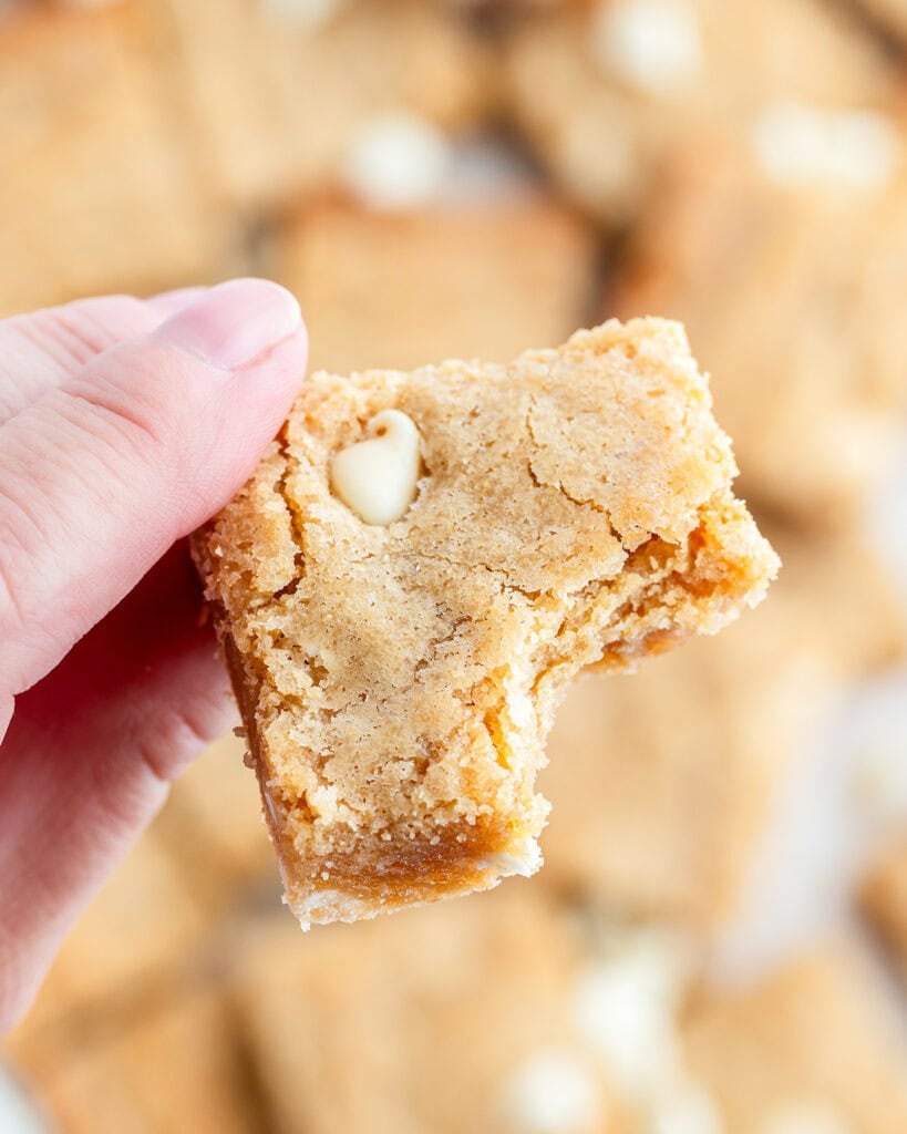 A hand holding a blondie with a bite out of it.