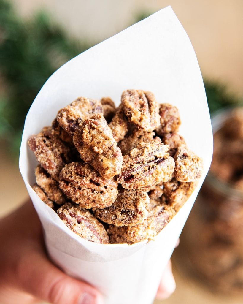 A hand holding a paper cone full of cinnamon roasted pecans.