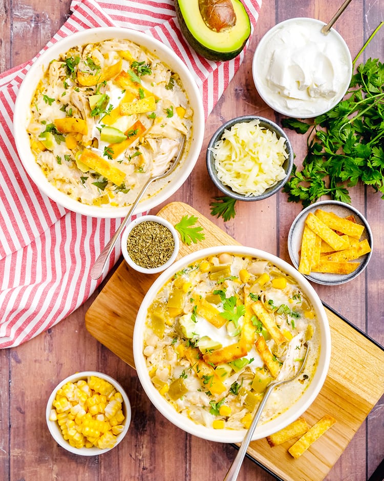 Two bowls of white chicken chili surrounded by little bowls of tortilla strips, cheese, and sour cream.