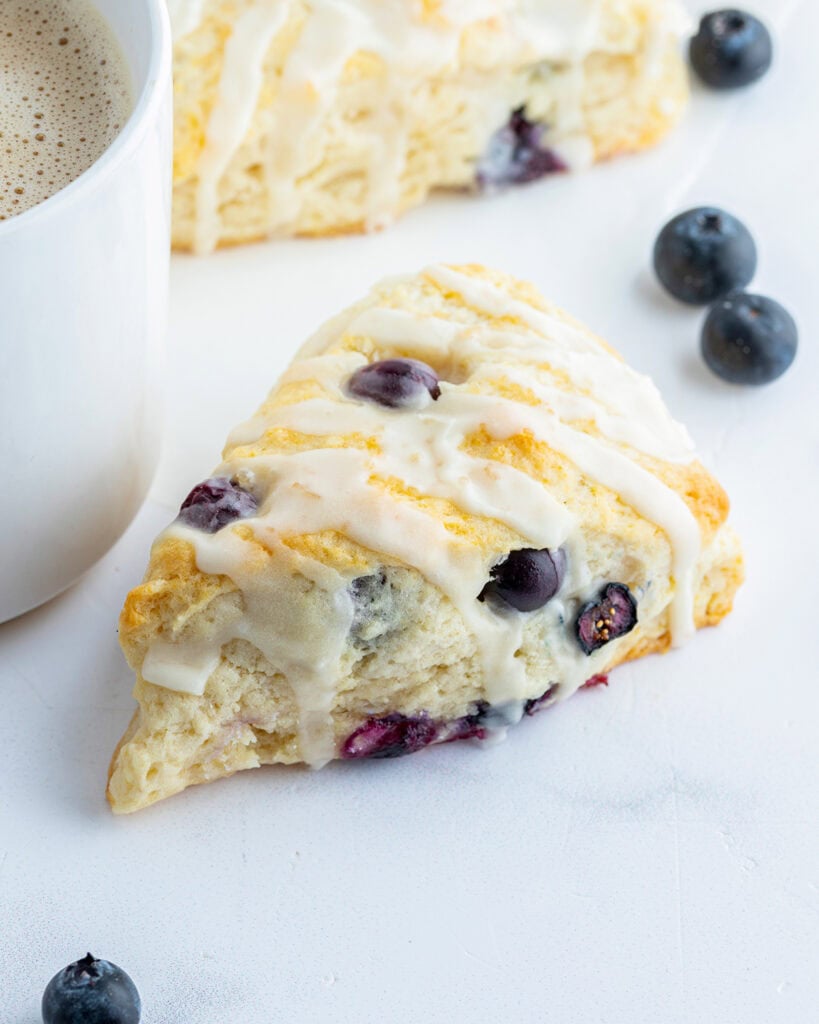A scone full of blueberries, next to a cup of tea.