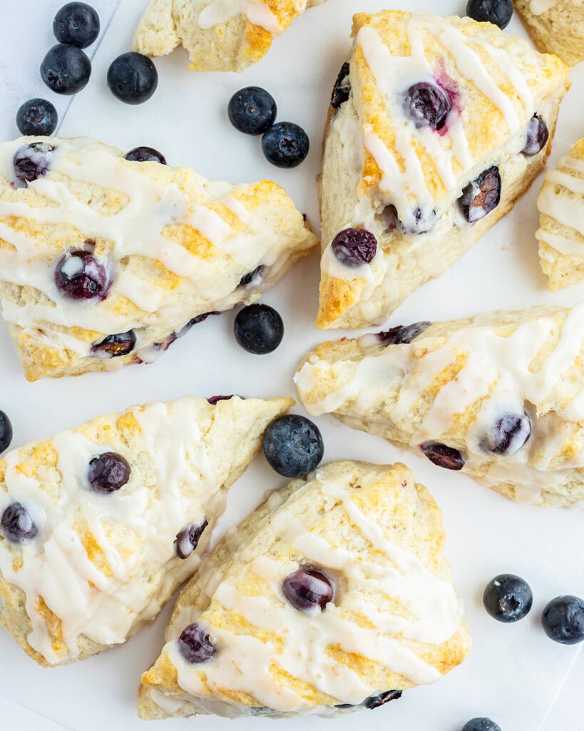 An overhead photo of scones full of blueberries and topped with a vanilla icing.