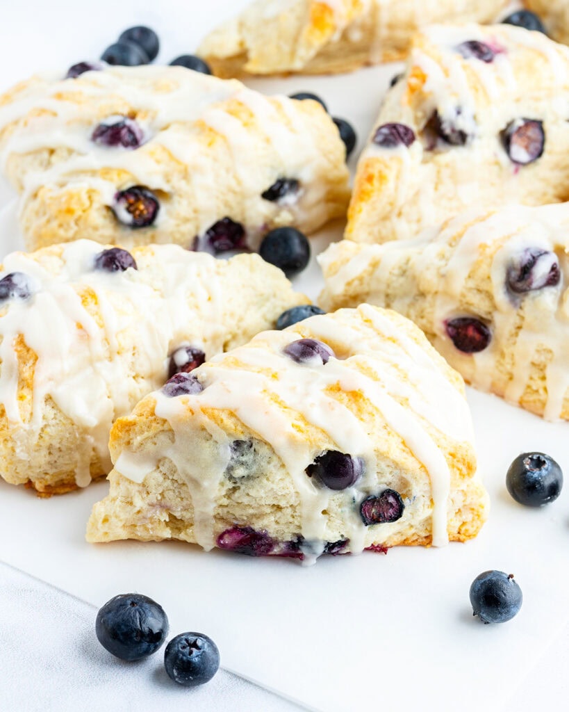 Blueberry scones pushed together near each other on a piece of parchment paper.