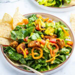 A bowl of chicken taco salad with some tortilla chips on the side.