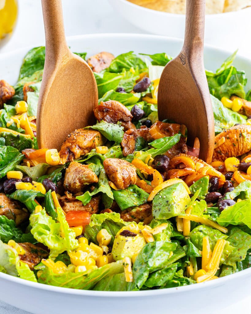 Two wooden spoons in a bowl of salad.