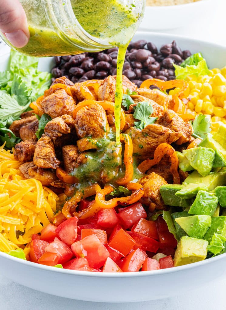 A green dressing being poured over a salad.
