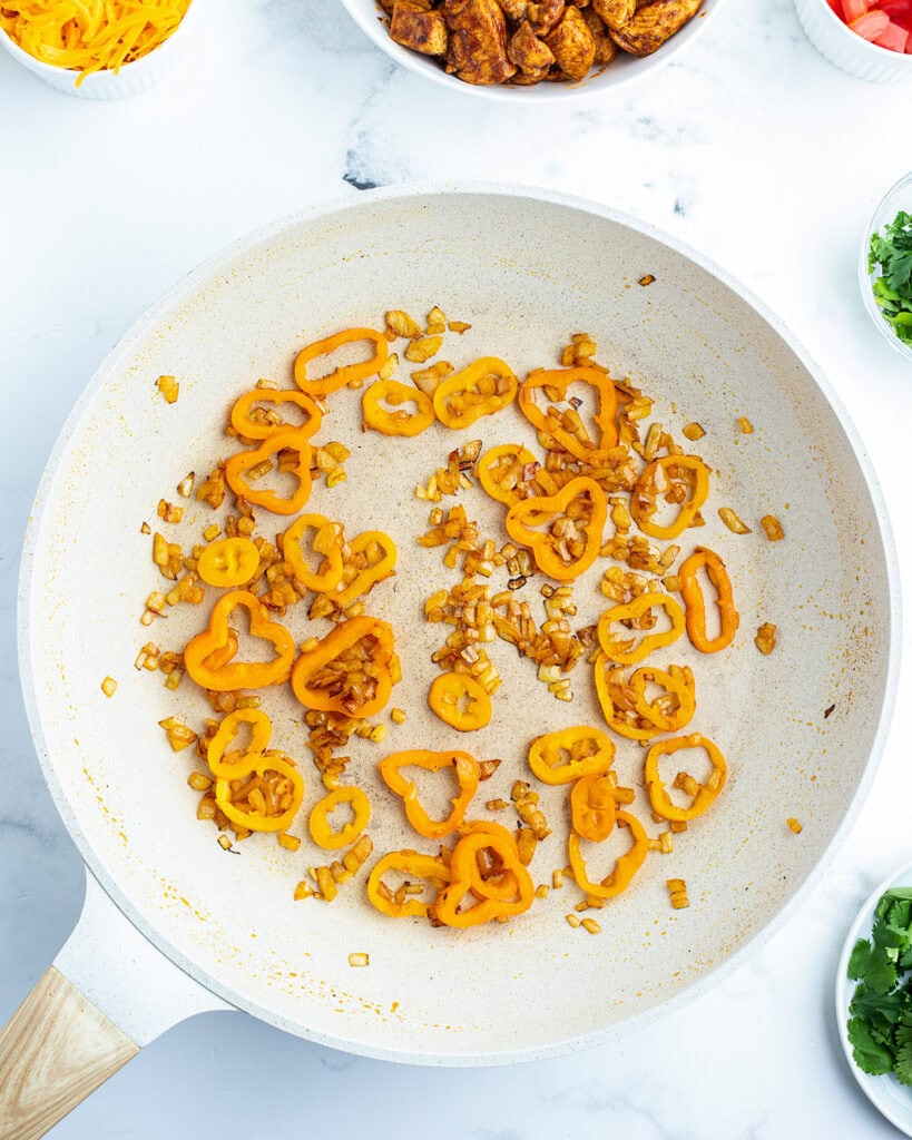 A saute pan with mini peppers and diced onions.
