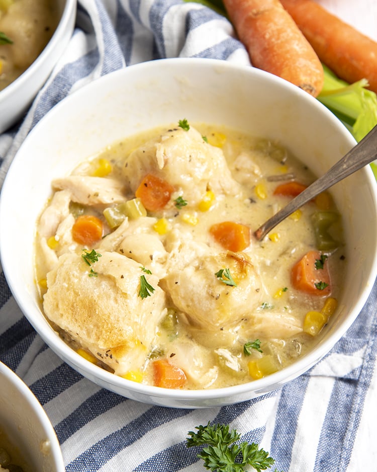 A bowl of easy chicken and dumplings with carrots and topped with parsley.