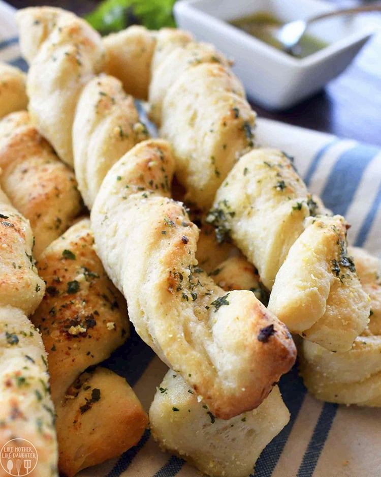 A close up of twisted bread sticks, that are baked and golden brown, and topped with fresh herbs.