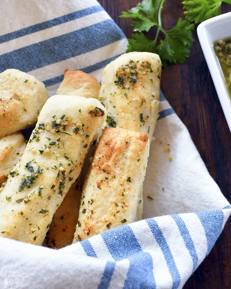 A close up photo of garlic bread sticks that are golden brown and topped with green chopped herbs.