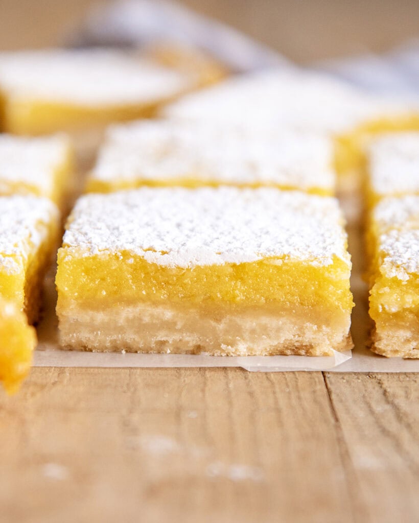 A side view of lemon bars with a shortbread crust, and lemon topping, and powdered sugar.