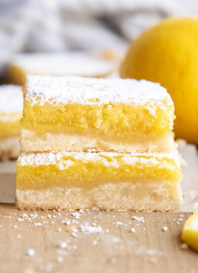 A side view of a stack of two lemon bars with a shortbread crust, and lemon topping, and powdered sugar.