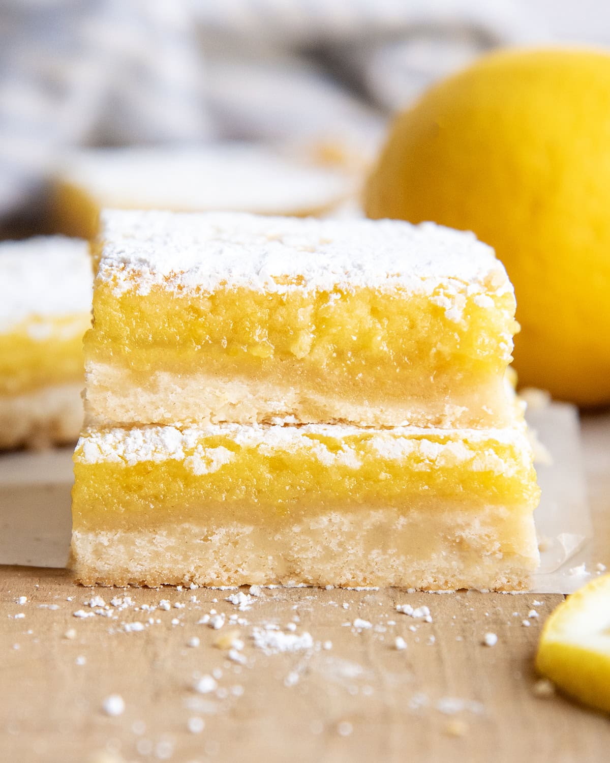 A side view of a stack of two lemon bars with a shortbread crust, and lemon topping, and powdered sugar.