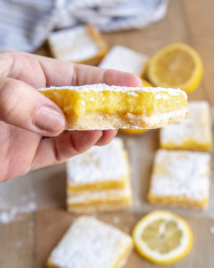 A and holding a lemon bar with a bite out of it.