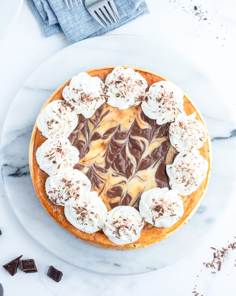 An above view of a marble cheesecake topped with dollops of whipped cream all around the edges.