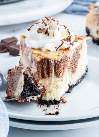 A plate of a vanilla and chocolate swirled cheesecake topped with whipped cream.