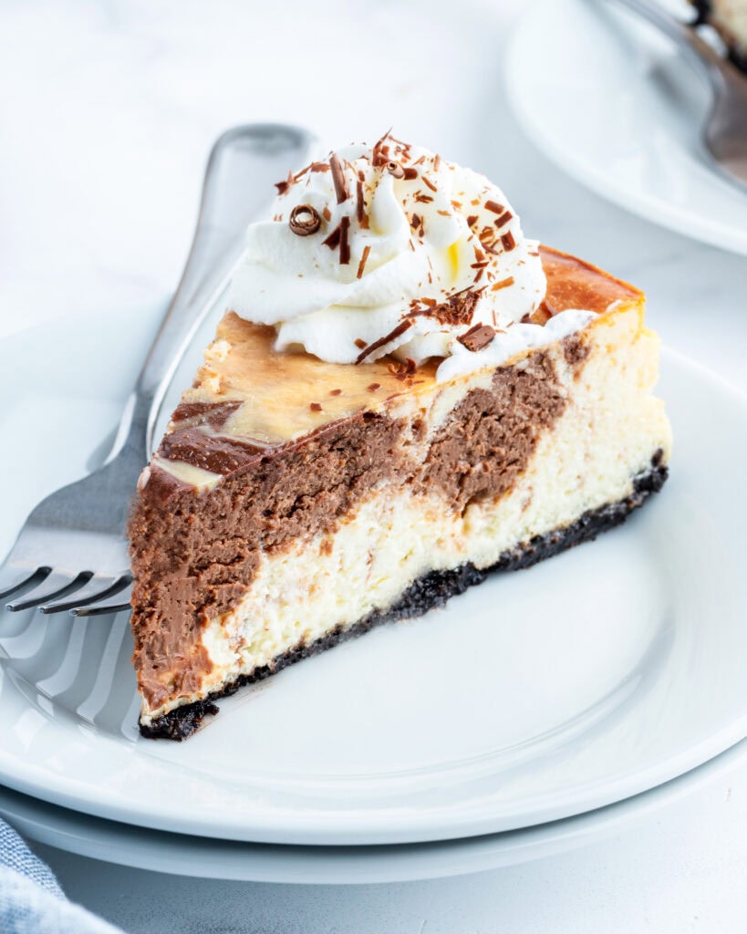 A slice of marble cheesecake topped with a dollop of whipped cream, on a white plate.
