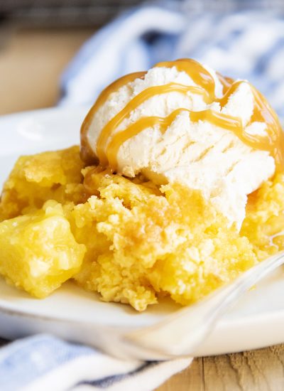 A serving of pineapple cobbler on a plate topped with vanilla ice cream and caramel syrup.