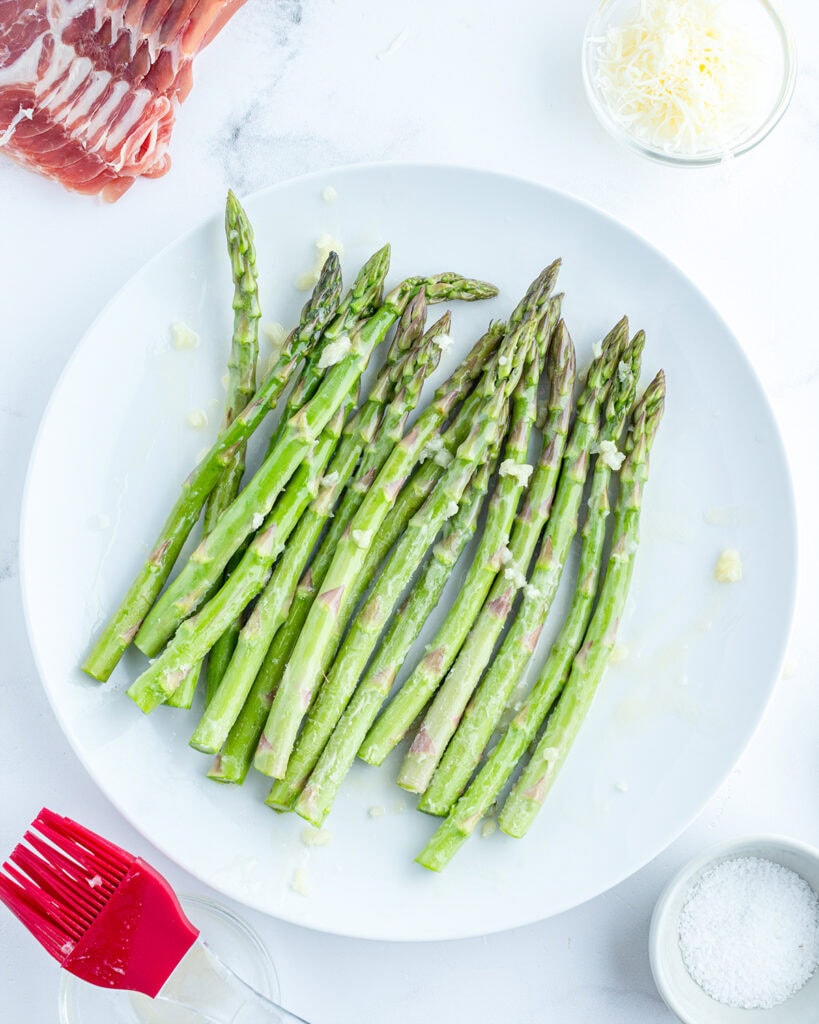 Raw asparagus stalks on a plate topped with melted butter.