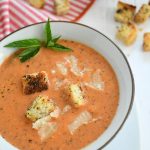 A bowl of tomato soup full of croutons and fresh parmesan.