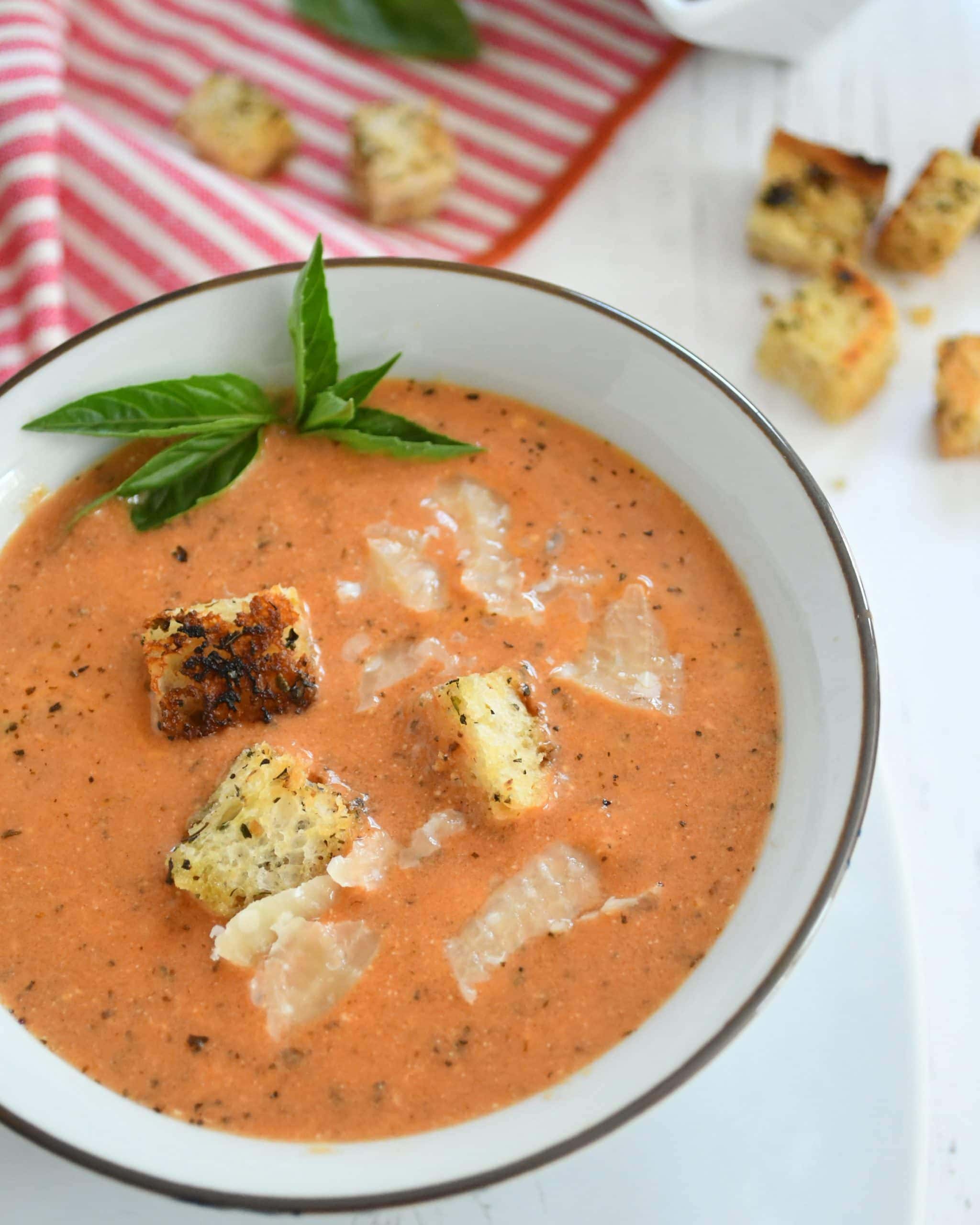 A bowl of tomato soup full of croutons and fresh parmesan.