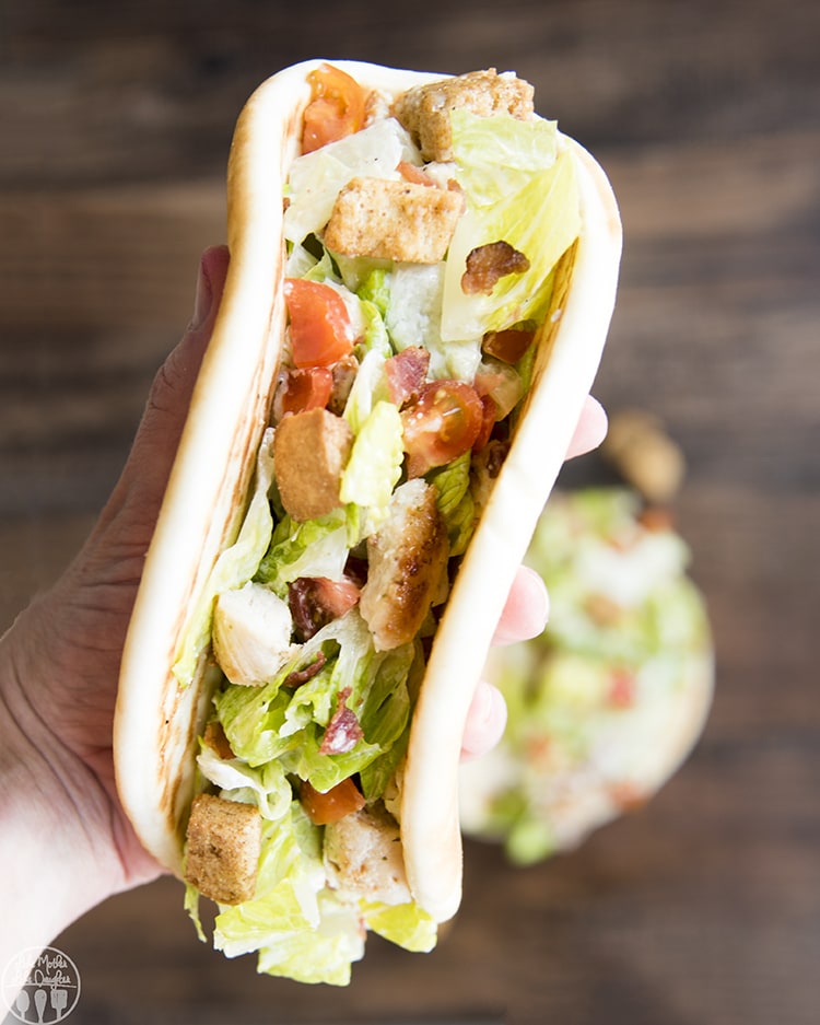 A hand holding a chicken caesar salad pita.