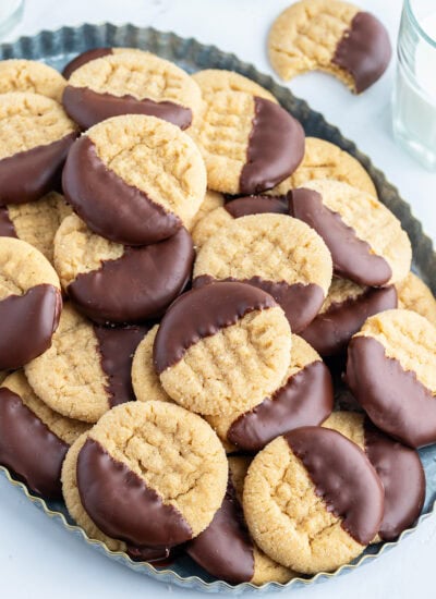 A platter of peanut butter cookies with a criss-cross pattern on them, and they are each dipped partially in melted chocolate.