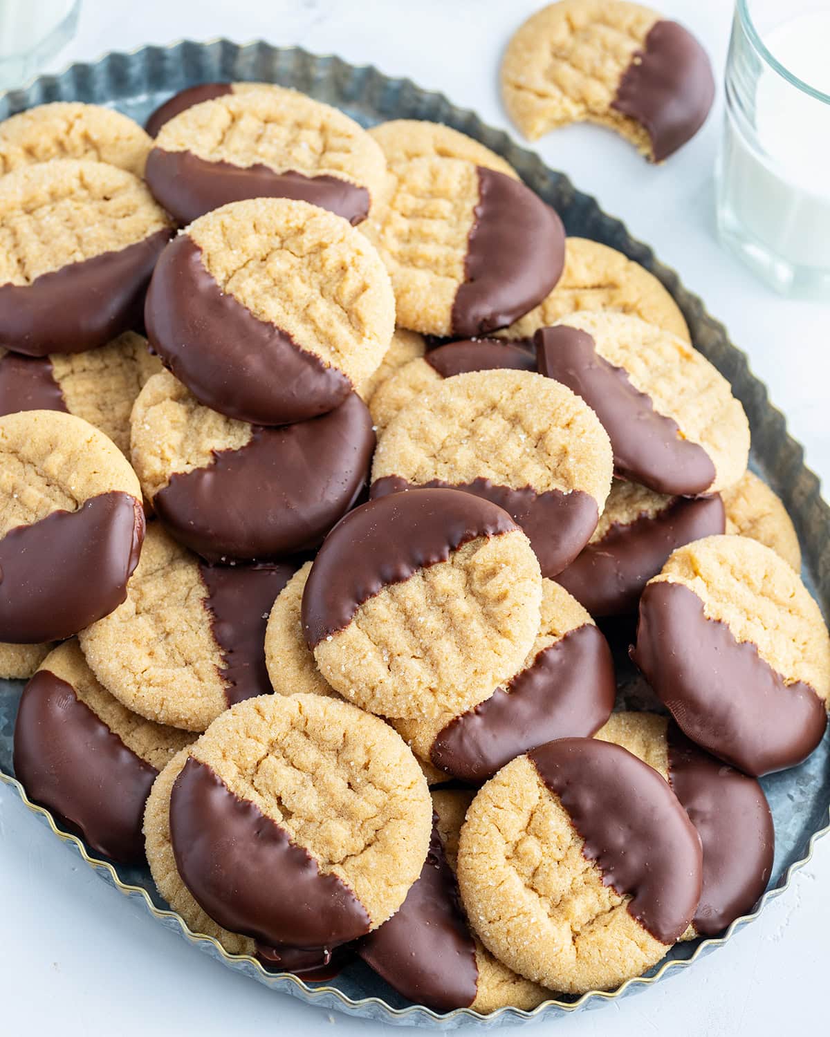 A platter of peanut butter cookies with a criss-cross pattern on them, and they are each dipped partially in melted chocolate.
