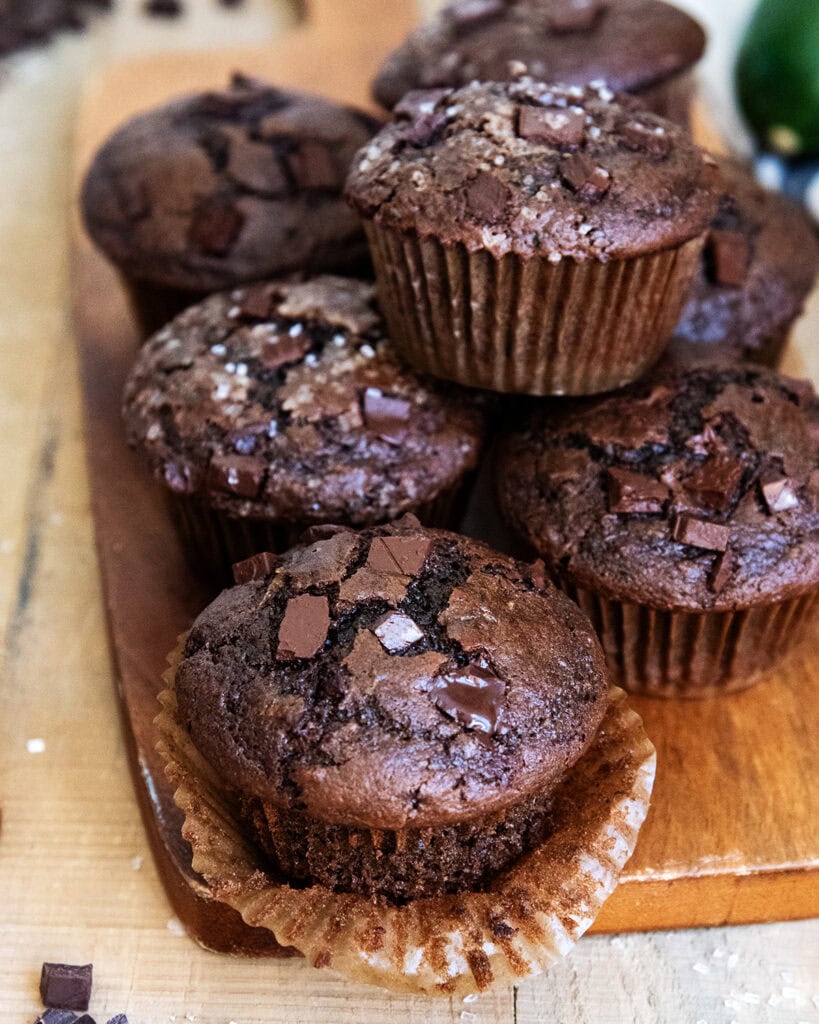 A pile of chocolate zucchini muffins on a wooden board.