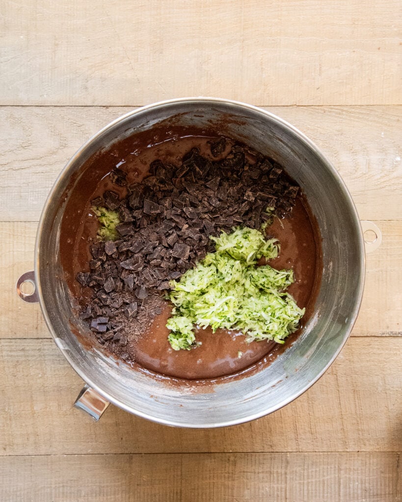 A bowl of chocolate muffin batter topped with zucchini and chocolate chunks.