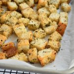 Italian seasoned croutons on parchment paper on a baking sheet on a cooling rack
