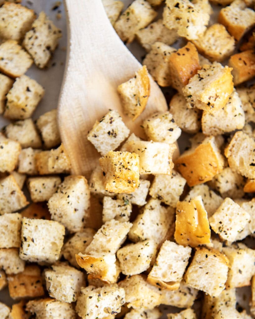 A wooden spatula lifting up some croutons.